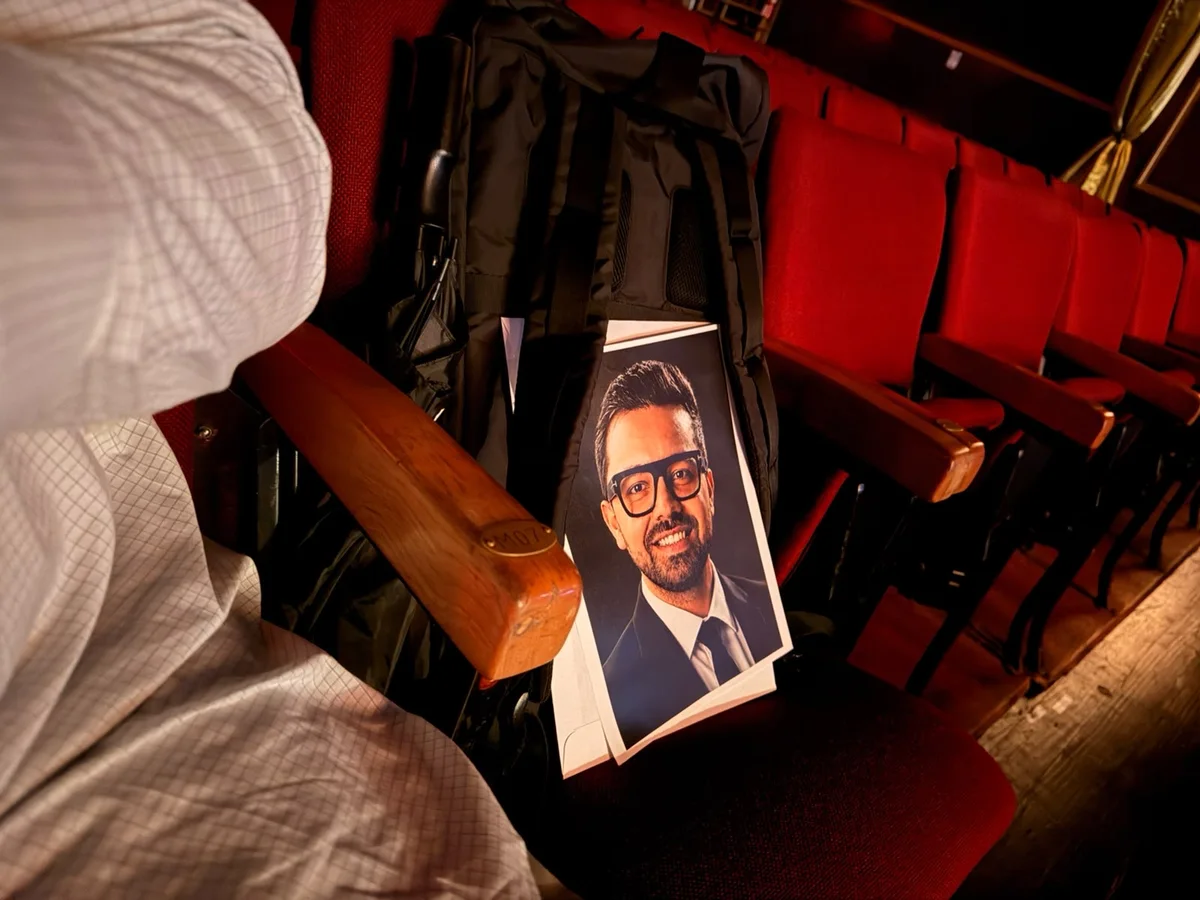 A printed portrait of Parul resting against a backpack on a red theatre seat.