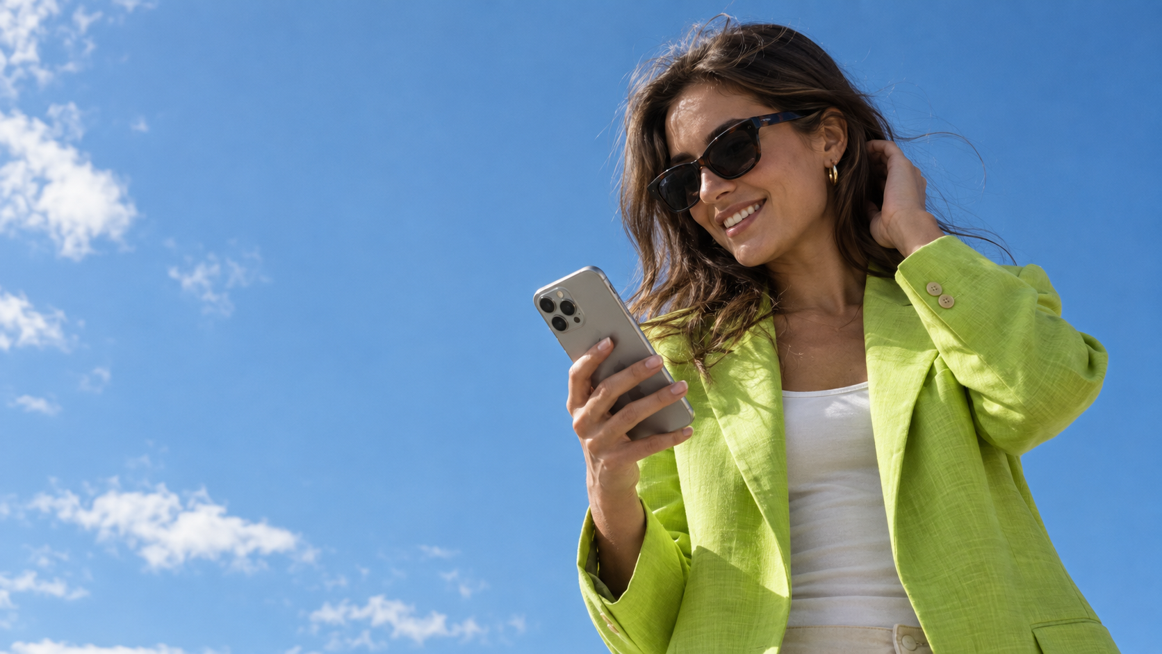 Une créatrice en blazer de lin vert lime consulte son téléphone sous un grand ciel bleu